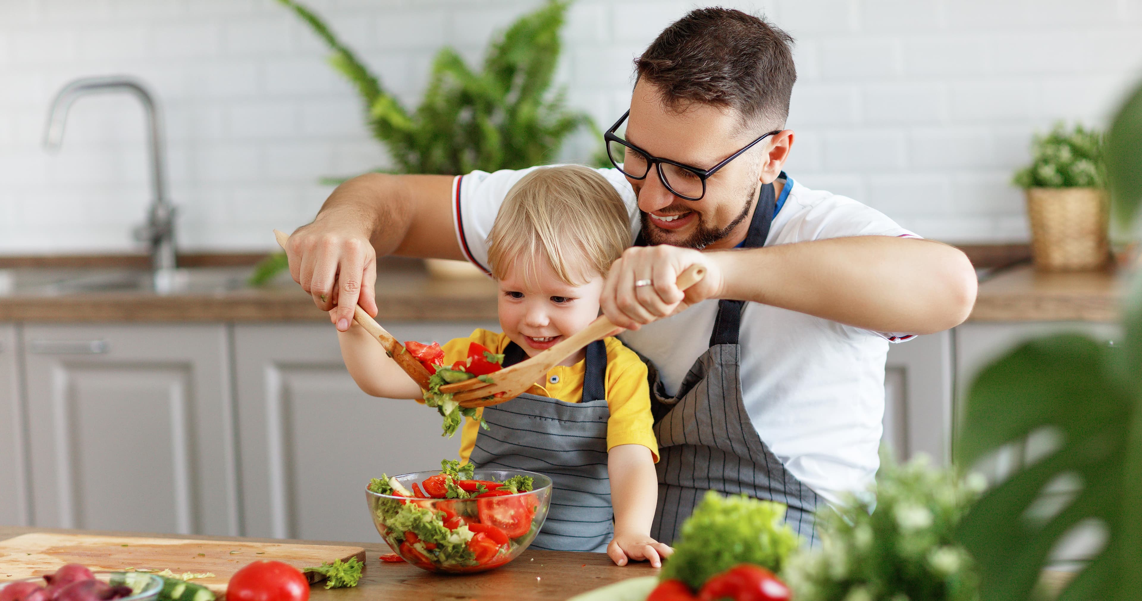 Man with his son sitting in front of him facing a chopping block and making a fresh salad.