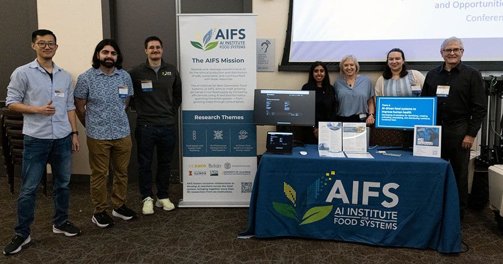 AIFS team, from left to right, includes Fangzhou Li, Ammar Ziadeh, Lukas Maximilian Masopust, Ashley Balley, Kristin Singhasemanon, Georgiana Prevost, and Steve Brown at the AIFS table at Research Expo with the AIFS banner and two computer screens on the table