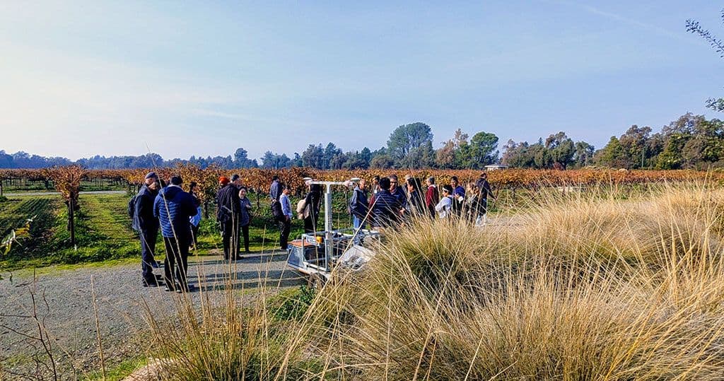 AgTech Workshop participants and instructors with a farm robot next to a vineyard